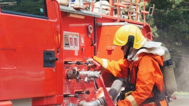 İtfaiyeci, itfaiye aracında yangın söndürücüyü söndürmek için ekipman hazırla. İtfaiyeci duman aleviyle savaşıyor. Yangın hortumu, tüp, kamyonda kimyasal köpük spreyi kullanıyor. İtfaiyeci sıkı bir şapka takıyor.