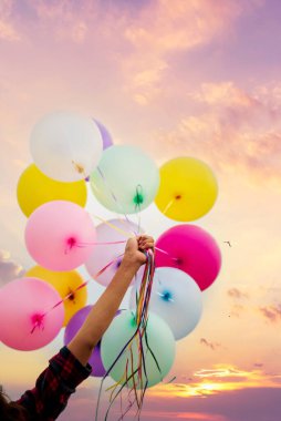 Dikey mor pastel gökyüzü kızı elinde balon tutuyor. Yeşil çayır menekşe arka planında koşan neşeli tatlı kız. Hava balonlarını tutan eller doğum günü partisinde açık havada mutlu mesut oynar.