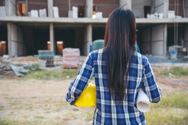 İnşaat mühendisi kadın işçi sanayisinde ekose gömlekli, beyaz kasketli, inşaat işçisi. Mimari mühendis kadın memur emlak projesine bakıyor.