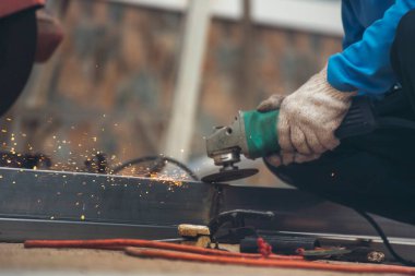 İnşaat işçisi elleri kaynak makineleri ile metal kıvılcımlar saçıyor. Erkek elleri koruyucu eldiven giyer. Alev metali, ateş demiri atölyesini keser. Çilingir kaynak makinesi kullanarak metal işlemini kesti