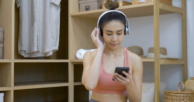 Mutlu Asyalı dansçı kadın kulaklık takıyor akıllı telefondan müzik dinliyor evdeki oturma odasında mutlu dans ediyor. Müzik terapisti, rahatlatıcı kadın. Neşeli sağIık, kadınlar iyi bir şekilde dans ediyor.