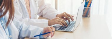 Sağlık hizmetleri ekip çalışmasını tartışan iki kadın doktor laboratuvarının afiş elleri. Panorama. İki Asyalı kadın doktor, reçeteli tıbbi muayenehane için fotokopi alanı olan dizüstü bilgisayar kullanıyorlar..