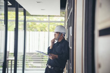 İnşaat mühendisi not yazıyor. İnşaat alanında mavi gömlekli güvenlik kasketi takıyor. Endüstriyel işçi erkek işçi. Mimarcı, mühendis, sivil konstrüksiyon gayrimenkul çiziyor.