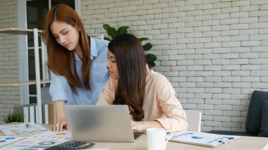 Finansal grafik grafiklerini okuyan iki Asyalı kadın pazarlama verilerini analiz etmeyi planlıyor. Asyalı takım çalışanı ofis firması. Şirket masasında dizüstü bilgisayarla iki iş kadını buluşması..