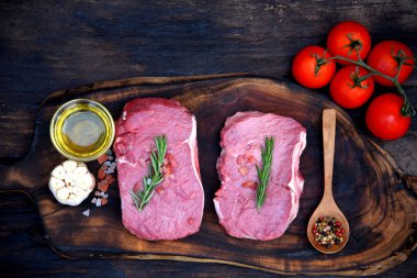 Biberiye, tuz, sarımsak, domates, karabiber ve zeytinyağı ile ahşap masa arkasında çiğ et bifteği taze organik malzeme. Biftek ve çiğ et için ahşap tabakta et.