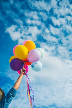 Dikey neşeli kız elinde balonlarla yeşil çayır üzerinde koşuyor mutlulukla mavi bulutlu gökyüzü. Doğum günü partisinde hava balonları tutan eller dışarıda mutlu zamanlar geçirir.