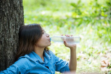 Su içen genç bir kadın açık hava parkı yolcusu. Asyalı kadın içme suyu şişesi sağlıklı insan mutlu bir gülümseme. Mutluluk. Güzel Asyalı Çinli kadınlar ellerinde maden suyu şişesi yaşam tarzı tutuyorlar.