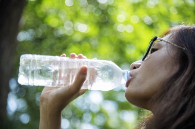Su içen genç bir kadın açık hava parkı yolcusu. Asyalı kadın içme suyu şişesi sağlıklı insan mutlu bir gülümseme. Mutluluk. Güzel Asyalı Çinli kadınlar ellerinde maden suyu şişesi yaşam tarzı tutuyorlar.