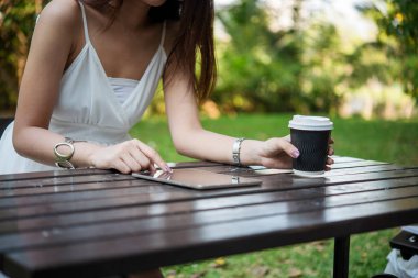 Yeşil Park 'ta kahve içen bir kadın elinde sıcak tek kullanımlık bardak tutuyor. Happy rahatla güzel Asyalı kadın gülümseyen yüz açık hava bahçesinde duruyor. Genç kadınlar doğanın tadını çıkarıyorlar Özgürlük yaşam tarzı.