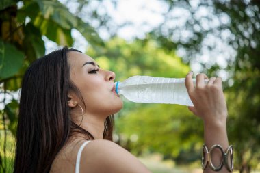 Su içen genç bir kadın açık hava parkı yolcusu. Asyalı kadın içme suyu şişesi sağlıklı insan mutlu bir gülümseme. Mutluluk. Güzel Asyalı Çinli kadınlar ellerinde maden suyu şişesi yaşam tarzı tutuyorlar.