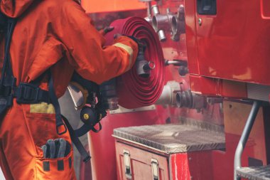 İtfaiyeci, itfaiye aracında yangın söndürücüyü söndürmek için ekipman hazırla. İtfaiyeci duman aleviyle savaşıyor. Yangın hortumu, tüp, kamyonda kimyasal köpük spreyi kullanıyor. İtfaiyeci sıkı bir şapka takıyor.