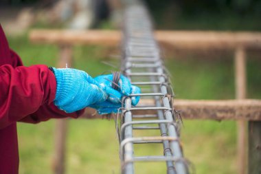 İnşaatçıların elleri çelik telleri büküyor beton işçiliğini destekliyor. Kerpeten kullanan işçi elleri demir tel kullanıyor. Açık hava işçisi, tel bükme pensesi kullanıyor, inşaat işi yapıyor.