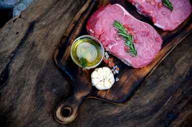 Manzaralı çiğ et eti ızgarası ahşap tahtada domuz eti barbeküsü. Biftek, batı mutfağı. Bitki, et, biber, zeytin, sarımsak, biberiye, ahşap tabakta tuzlu biberiye..