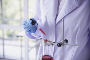 Kimyasal test tüpü tutan bilim laboratuarındaki bilim kadını. Cam tüp tanısı için kırmızı damlayı tutan laboratuvar teknisyeni kan örneği. Tıbbi kimya testinde çalışan Asyalı kadın bilim adamı