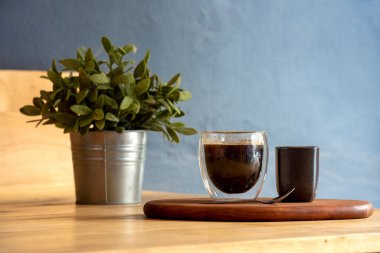 Ahşap ofis masasındaki sıcak sade kahve fincanı masa mavisi süsleme masası arka planı. Baharda ofis ahşap masa bahçesinde bir fincan Siyah Çay Yeşil Saksı bitkisi. Taze ev işyeri dekorasyon masası