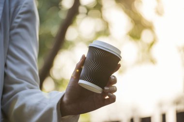 Yeşil Park 'ta kahve içen bir kadın elinde sıcak tek kullanımlık bardak tutuyor. Happy rahatla güzel Asyalı kadın gülümseyen yüz açık hava bahçesinde duruyor. Genç kadınlar doğanın tadını çıkarıyorlar Özgürlük yaşam tarzı.