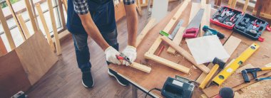 Banner DIY zanaatkar Asyalı adam ahşap yığını marangoz eşya masasında çalışıyor. Banner Mimarı elinde cetvelle ev gelişimini ölçüyor. Kopya alanı olan marangoz inşaat atölyesi