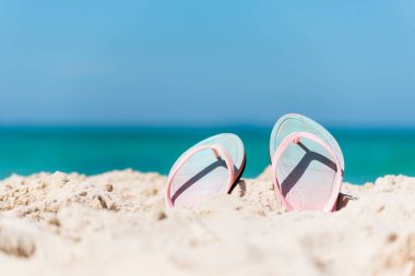 Plaj tatili için sarı sandaletli lastik ayakkabı. Güneşli bir günde deniz dalgası olan tropik yaz plajı. Terlikler açık havada, kumsalda beyaz dalgalı mavi deniz. Yaz tropik plajı