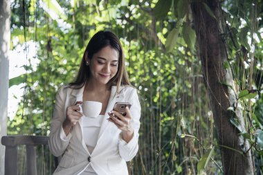Yeşil Park 'ta kahve içen bir kadın elinde sıcak tek kullanımlık bardak tutuyor. Happy rahatla güzel Asyalı kadın gülümseyen yüz açık hava bahçesinde duruyor. Genç kadınlar doğanın tadını çıkarıyorlar Özgürlük yaşam tarzı.
