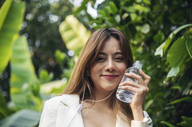 Su içen genç bir kadın açık hava parkı yolcusu. Asyalı kadın içme suyu şişesi sağlıklı insan mutlu bir gülümseme. Mutluluk. Güzel Asyalı Çinli kadınlar ellerinde maden suyu şişesi yaşam tarzı tutuyorlar.