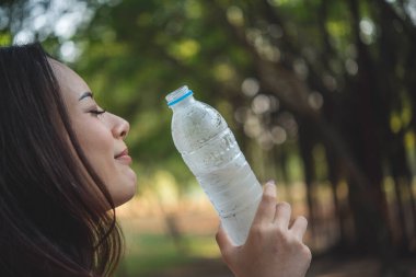 Su içen genç bir kadın açık hava parkı yolcusu. Asyalı kadın içme suyu şişesi sağlıklı insan mutlu bir gülümseme. Mutluluk. Güzel Asyalı Çinli kadınlar ellerinde maden suyu şişesi yaşam tarzı tutuyorlar.