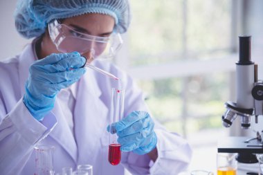 Kimyasal test tüpü tutan bilim laboratuarındaki bilim kadını. Cam tüp tanısı için kırmızı damlayı tutan laboratuvar teknisyeni kan örneği. Tıbbi kimya testinde çalışan Asyalı kadın bilim adamı