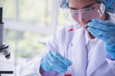 Kimyasal test tüpü tutan bilim laboratuarındaki bilim kadını. Cam tüp tanısı için kırmızı damlayı tutan laboratuvar teknisyeni kan örneği. Tıbbi kimya testinde çalışan Asyalı kadın bilim adamı