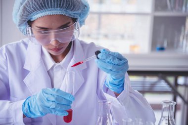 Kimyasal test tüpü tutan bilim laboratuarındaki bilim kadını. Cam tüp tanısı için kırmızı damlayı tutan laboratuvar teknisyeni kan örneği. Tıbbi kimya testinde çalışan Asyalı kadın bilim adamı