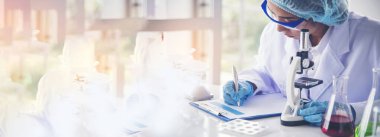 Asyalı kadın bilim adamı tıp laboratuarında bilimsel mikroskoba bakarak notlar yazıyor. Panorama biyoloji kimya laboratuvarı. Kopya alanı ile mikroskop kullanan Asyalı kadın teknisyen laboratuvarı