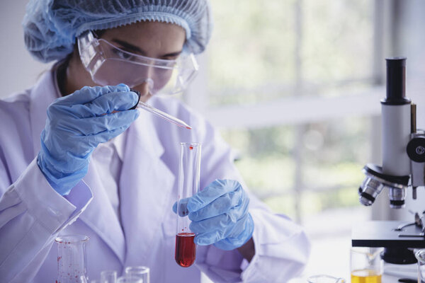 Ученая женщина проводит химические испытания стеклянной трубки лаборатории. Лаборант держит красную каплю в стеклянной трубке для диагностики образца крови. Азиатская женщина-ученый