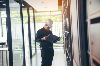 İnşaat mühendisi not yazıyor. İnşaat alanında mavi gömlekli güvenlik kasketi takıyor. Endüstriyel işçi erkek işçi. Mimarcı, mühendis, sivil konstrüksiyon gayrimenkul çiziyor.