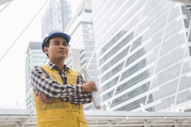 Banner İnşaat Mühendisi Bina planında mavi gömlekli güvenlik önlüğü giyer inşaat sahasındaki fabrikada beyaz şapka giyer. Panorama Mimarlık erkek inşaat mühendisi kopya alanı ile planlara bakıyor.