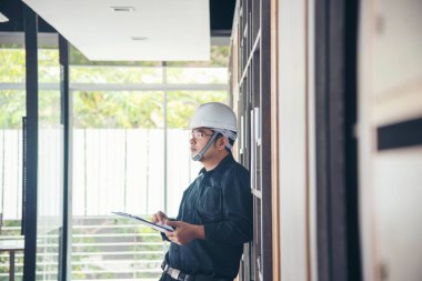 İnşaat mühendisi not yazıyor. İnşaat alanında mavi gömlekli güvenlik kasketi takıyor. Endüstriyel işçi erkek işçi. Mimarcı, mühendis, sivil konstrüksiyon gayrimenkul çiziyor.