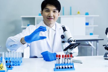 Bilim adamı bilim laboratuarındaki mikroskop araştırmalarını inceliyor. Asyalı bilim adamı mikrobiyoloji mikroskop laboratuvar ekipmanları kimya laboratuvarına bakıyor. Biyokimya araştırma aşısı konsepti
