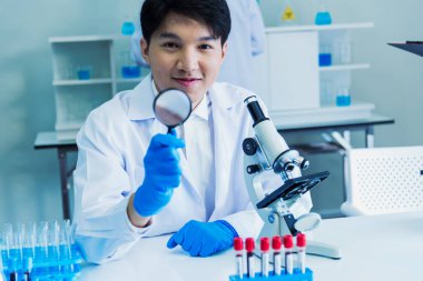 Bilim adamı bilim laboratuarındaki mikroskop araştırmalarını inceliyor. Asyalı bilim adamı mikrobiyoloji mikroskop laboratuvar ekipmanları kimya laboratuvarına bakıyor. Biyokimya araştırma aşısı konsepti