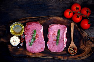 Manzaralı çiğ et eti ızgarası ahşap tahtada domuz eti barbeküsü. Biftek, batı mutfağı. Bitki, et, biber, zeytin, sarımsak, biberiye, ahşap tabakta tuzlu biberiye..