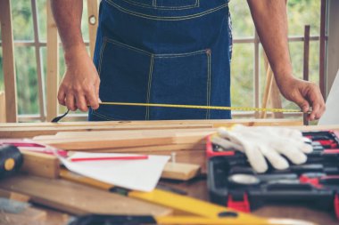 Ahşap yığını marangozluk masasında çalışan Asyalı bir zanaatkar. Mimar eller cetvel ölçü çekici ev geliştirme kullanıyor. Ahşap marangoz inşaat atölyesini tamir ediyor.