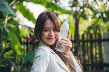 Su içen genç bir kadın açık hava parkı yolcusu. Asyalı kadın içme suyu şişesi sağlıklı insan mutlu bir gülümseme. Mutluluk. Güzel Asyalı Çinli kadınlar ellerinde maden suyu şişesi yaşam tarzı tutuyorlar.