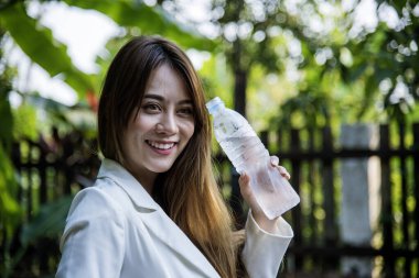 Su içen genç bir kadın açık hava parkı yolcusu. Asyalı kadın içme suyu şişesi sağlıklı insan mutlu bir gülümseme. Mutluluk. Güzel Asyalı Çinli kadınlar ellerinde maden suyu şişesi yaşam tarzı tutuyorlar.