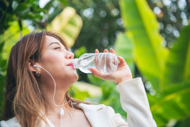 Su içen genç bir kadın açık hava parkı yolcusu. Asyalı kadın içme suyu şişesi sağlıklı insan mutlu bir gülümseme. Mutluluk. Güzel Asyalı Çinli kadınlar ellerinde maden suyu şişesi yaşam tarzı tutuyorlar.