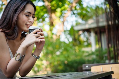 Yeşil Park 'ta kahve içen bir kadın elinde sıcak tek kullanımlık bardak tutuyor. Happy rahatla güzel Asyalı kadın gülümseyen yüz açık hava bahçesinde duruyor. Genç kadınlar doğanın tadını çıkarıyorlar Özgürlük yaşam tarzı.