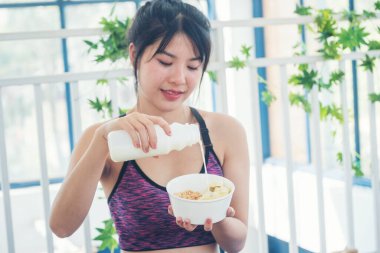 Asyalı kadınlar güler, kameralı sağlık hizmetleri yaşam tarzına bakarlar. Güzel bayan az yağlı süt içen laktozsuz süt. Kadın elleri beyaz bir bardak süt tutuyor şişeden dökülüyor