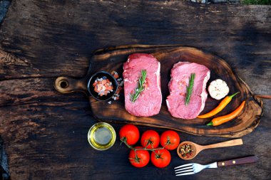 Manzaralı çiğ et eti ızgarası ahşap tahtada domuz eti barbeküsü. Biftek, batı mutfağı. Bitki, et, biber, zeytin, sarımsak, biberiye, ahşap tabakta tuzlu biberiye..