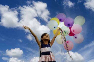 Balon tutan neşeli güzel kadın yeşil parktaki büyük ağacın altında mutlu mesut oturuyor. Kadın Eller 'in elinde canlı hava balonları var. Doğum günü partisinde oynuyorlar. Mutlu yaz mevsimi açık havada.