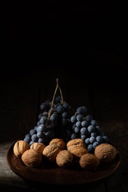 Ahşap bir masada, kil bir tabakta mavi üzüm ve fındık.