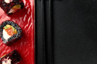 Japanese food: sushi, Roll with cuttlefish ink, mango, salmon, tobiko caviar, avocado. Black background