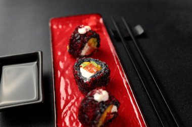 Japanese food: sushi, Roll with cuttlefish ink, mango, salmon, tobiko caviar, avocado. Black background