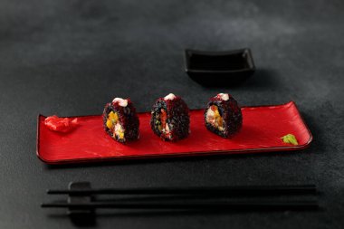 Japanese food: sushi, Roll with cuttlefish ink, mango, salmon, tobiko caviar, avocado. Black background