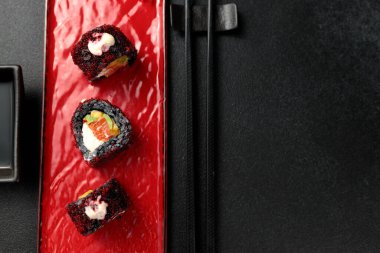 Mürekkepbalığı mürekkebi, mango, somon, tobiko havyarı ve avokado içeren suşi rulosu siyah arka planda sergilenir. Japon mutfağının renkli ve lezzetli bir temsili, stok fotoğrafçılığı için mükemmel..