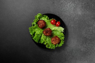 Lezzetli kızarmış pirzolalar, olgun domates dilimleriyle süslenmiş kıvırcık kıvırcık marul yatağında servis ediliyor. Hepsi de dramatik bir siyah arka planda sunuluyor. Yiyeceklerle ilgili tasarımlar, yemek blogları ya da restoran menüleri için mükemmel.